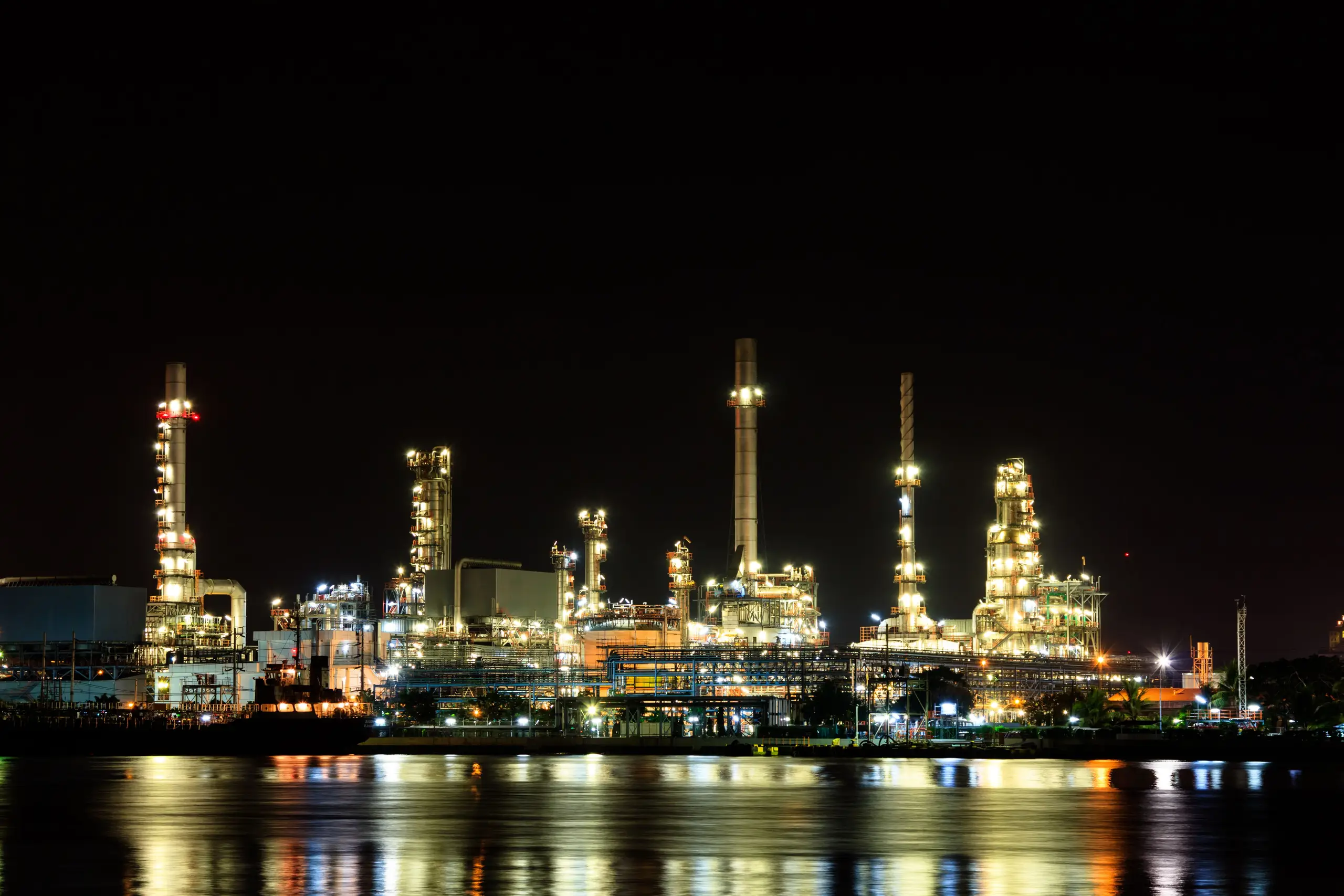 Oil refinery lit up at night, reflected in the water
