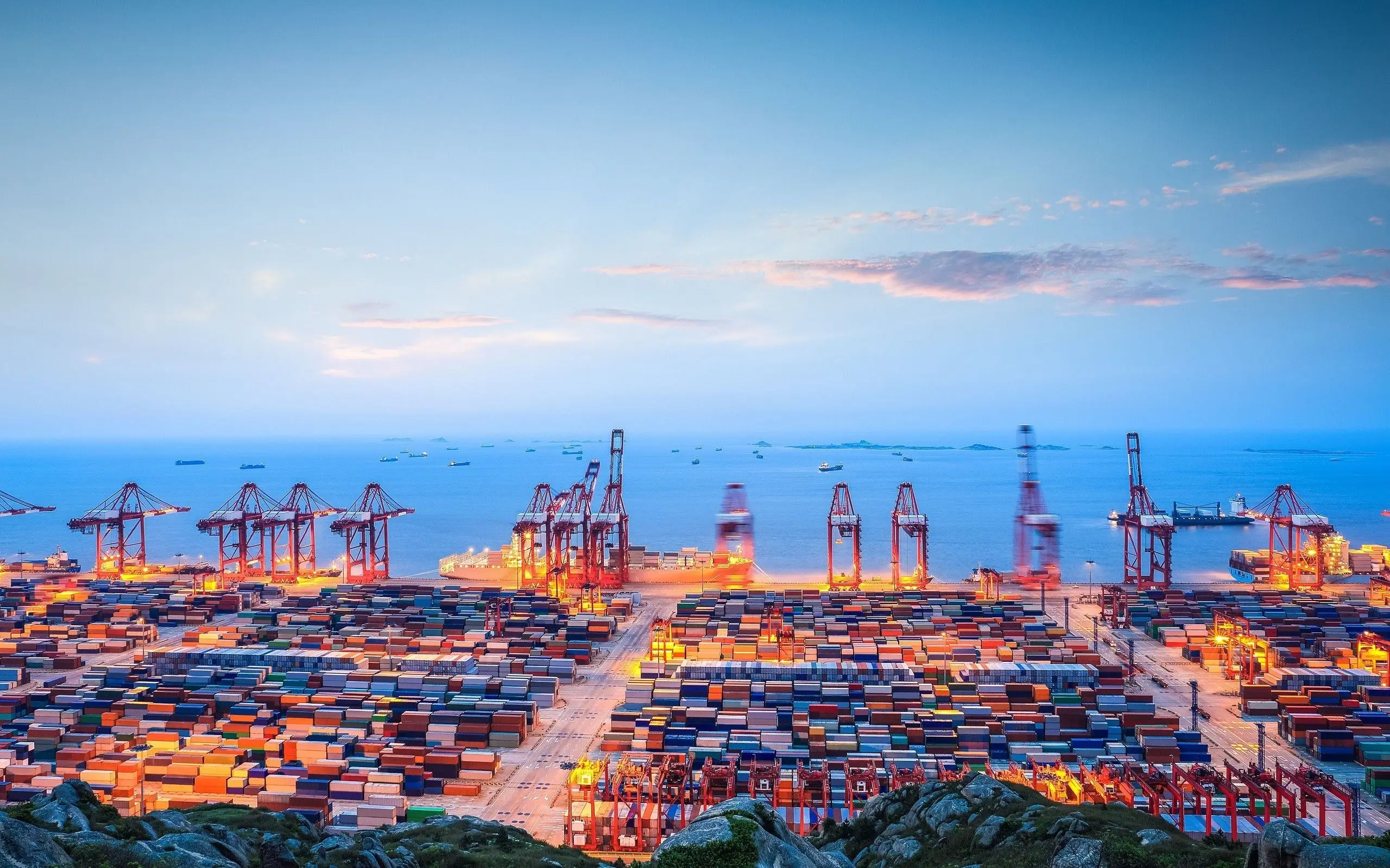 Port de containere la apus, cu macarale și containere stivuite lângă mare